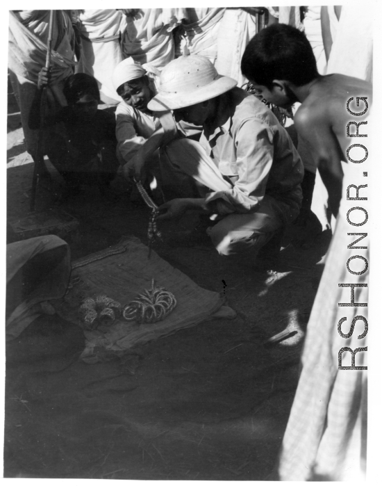 A GI negotiates for metal jewelry in India.  Scenes in India witnessed by American GIs during WWII. For many Americans of that era, with their limited experience traveling, the everyday sights and sounds overseas were new, intriguing, and photo worthy.