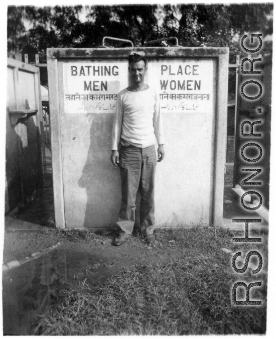 Irwin Schneckloth of 2005th Ordnance Maintenance Company, 28th Air Depot Group, poses with curiosity in front of public shower stall, likely in India. During WWII.