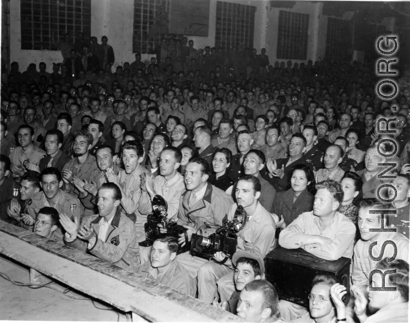 An eager audience of Chinese and American military personnel, along with Chinese civilians, view a performance in China during WWII. 