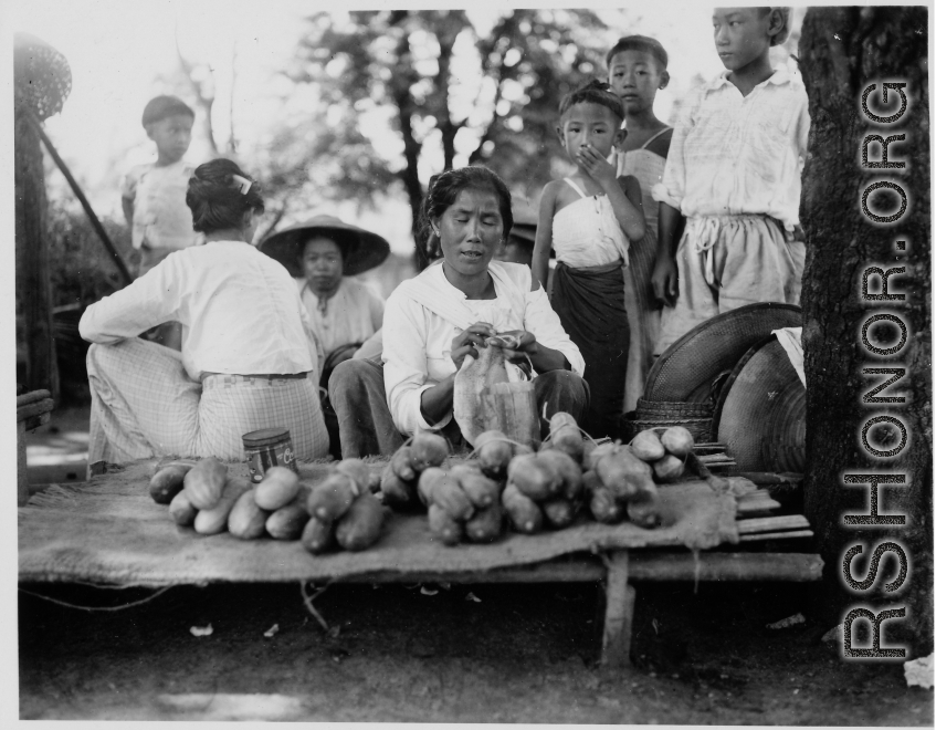 A woman sells cucumbers or something similar in Burma.  Local people in Burma near the 797th Engineer Forestry Company.  During WWII.
