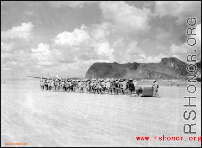 Laborers pull roller at Liuzhou during WWI, in 1945. A C-54 transport plane can be seen in the distance.