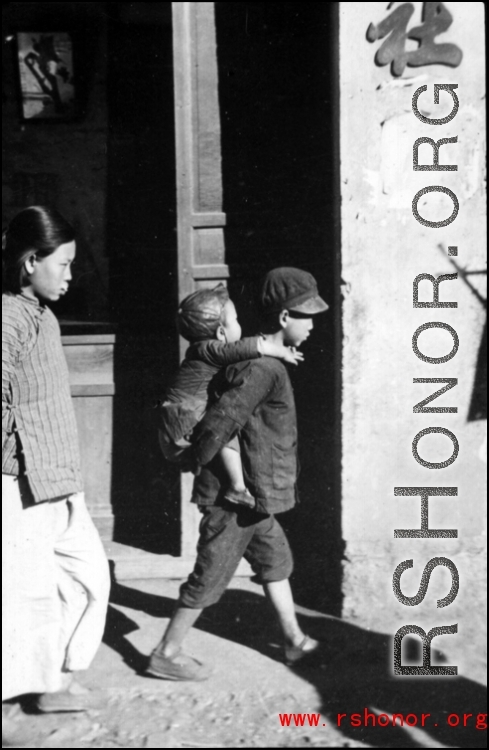 Older brother carries younger brother in a Chinese town during WWII. 