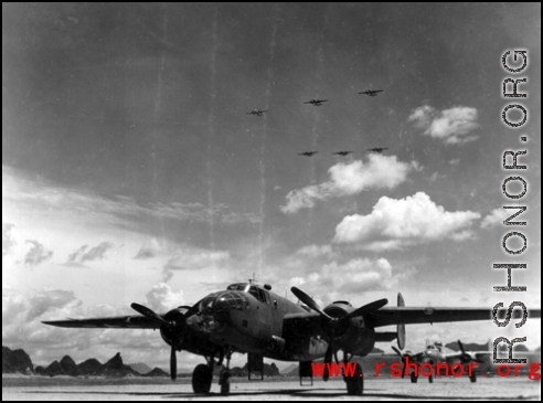 A B-25 on the ground at an American air base in Guangxi province, China, during WWII, with six B-25s flying in formation overhead.