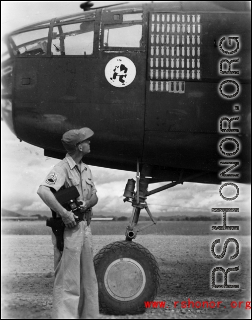 An American aircrew member observes the masking for three new mission symbols on the side of a B-25C at an airbase China. The "Mr. Jiggs" insigne of the 11th Bomb Squadron is visible, as well the previous sixty-three mission symbols.  
