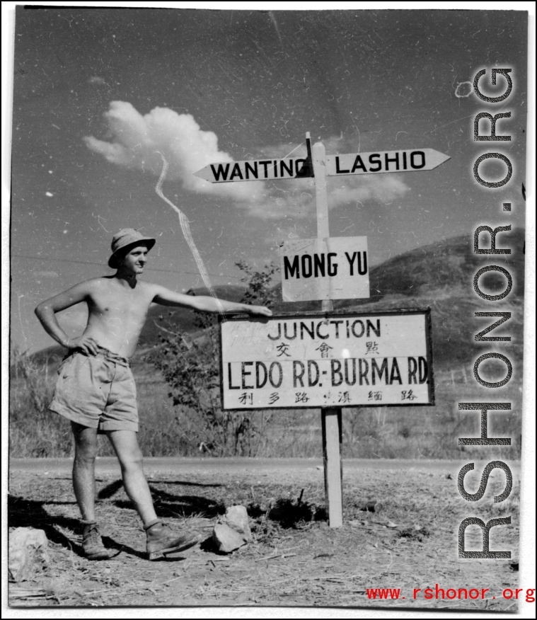 GI leans against sign at junction of Ledo Road and the Burma Road, during WWII.