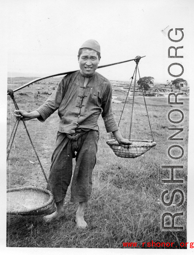A farmer poses with a shoulder pole near an American air base in Yunnan, China, during WWII.