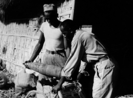 Two African-American soldiers load artillery shells into canvas-wrapped bamboo baskets for transport in the CBI during WWII.