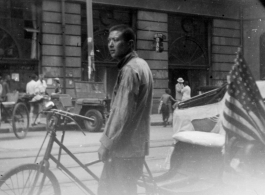Pedal-taxi driver with American flag. Probably after the end of war, in a large city like Shanghai.