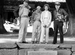 Americans in the China--armed with pistols and cameras--pose under the shade of large ancient trees outside a temple building. During WWII.