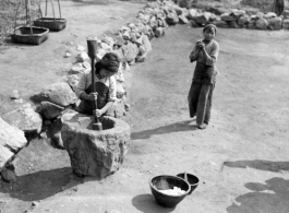 Local children laboring in China, Yunnan province, with a large mortar and pestle, either husking dry grain or mashing cooked rice so something similar. During WWII.