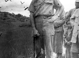 Elmer Bukey poses for a photo with some Chinese friends and a Thompson submachine gun, standing by a rice paddy, at Liangshan China, during WWII.