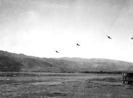 Several P-40 fighters pass over the runway and begin a "break out" to land at Yangkai, Yunnan province. The nose guns of an American B-25H bomber are visible at the far right of this picture taken in the CBI.