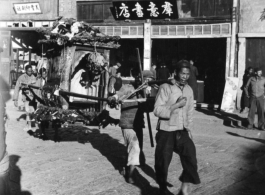 Men tote a decorated sedan chair used to carry the bride during weddings. In China, during WWII.