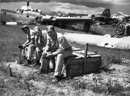 Three American GIs sitting on a discarded latrine box in front of wrecked American warplanes (including a B-24) in a boneyard at the base. An aircraft tail #349752 is in the background. Note men walking on wing of aircraft in background, undoubtedly engaged in salvage on the wing. In Yunnan, China, during WWII.