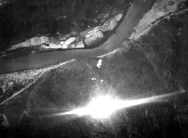 Bombing of small riverside town likely in SW China (esp. Guangxi), but possibly in Burma, or French Indochina. During WWII. Signs of previous bombings are visible about, including destroyed houses along the main road, and bomb craters here and there. The bright white spot is the arc flash of a bomb explosion, caught exactly at the right time, a another explosion is starting just above it.