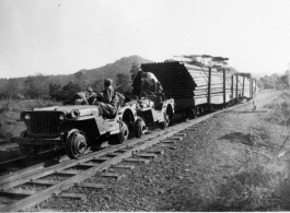 Two jeeps, fitted with steel wheels that fit the rail tracks, pull cars loaded with oil pipes. In Burma.  During WWII.  797th Engineer Forestry Company.