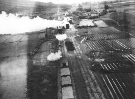 "It won't be long now! Watch bombs in air..."  This train was wiped out with low level bombs & gunfire. Note on back of the photo reads: Three track RR sliding with 17 cars and locomotive, which is destroyed, note wreckage from bomb bursts and quantity of escaping steam. 3 cars probably destroyed, more damaged. Two of track torn up by bomb bursts, hole from strafing is visible on extreme left track.  This should be Van Trai Station, French Indochina.