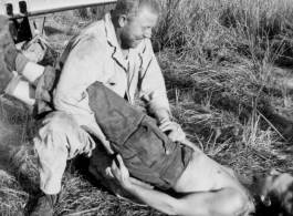 Leo Spearence and John Schuhart (bearded) wrestle on ground. G. I. Clip standing on wing of discarded fighter plane. Likely in Burma. 2005th Ordnance Maintenance Company,  28th Air Depot Group.