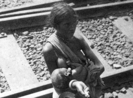 Breastfeeding beggar and infant along railroad tracks, likely in India, during WWII.