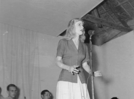 Singer at a USO show in Gushkara, India, during WWII.  The boxes in front of the band players are labeled 748th ROB (748th Railway Operating Battalion).