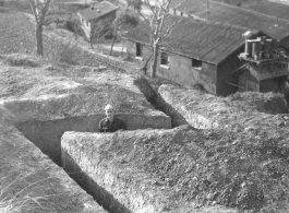 Flyer in air raid slit trench at Chanyi (Zhanyi), during WWII. Barracks behind.