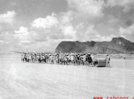 Laborers pull roller at Liuzhou during WWI, in 1945. A C-54 transport plane can be seen in the distance.