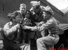 Smiling GIs pose with unhappy small child from poor family in China, during WWII.