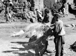 People in a local village in Yunnan province, China, threshing grain by striking the rice straw against old wooden wheels. During WWII.
