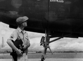 Combat Photographer Harold "Hal" Geer examines masking on bomb icons on a B-25  of the 11th Bomb Squadron (indicated by the "Mr. Jiggs" insignia) readying for painting to indicate three more bombing missions. In southwest China during WWII, as photographed by Selig Seidler, 16th Combat Camera Unit, in the CBI during WWII.