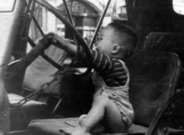 A Chinese toddler playing on a the driver's seat of a jeep in downtown Chengdu, China, during WWII.