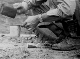 Member of the 988th Signal Service Battalion grabs a bite to eat along the Burma Road. "We quickly learned to heat cans of food on the engine, and have it warm and ready for a quick stop."