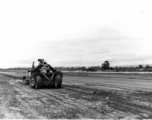 Mechanical grader flattens out a runway in the CBI during WWII, while C-47 moves in the background.