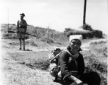 An elderly Chinese woman takes her lunch somewhere outside of Kunming, while a Nationalist guard is in the background. During WWII.