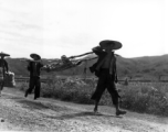 Men shoulder a stretcher, possibly carrying recovered human remains. During WWII, in China.
