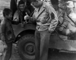 GI exchanges a thumbs up with kid in China, while other GIs observe from jeep. During WWII.