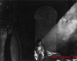 During WWII a boy sits in front of a stone tablet in the entry area of a temple or other building, probably in Yunnan province.