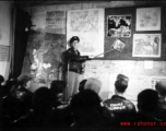 A pre-flight briefing for American flyers in China during WWII.. The maps on the wall behind the speaker clearly show Hong Kong harbor, which the Japanese controlled.