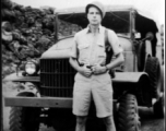 A GI stands in front on a truck on a road in the CBI during WWII.